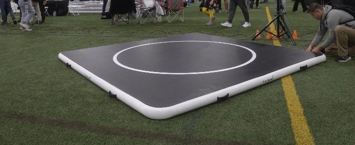 A 10 by 10 FlowMat set up on turf at an outdoor meet, with a coach kneeling at one corner