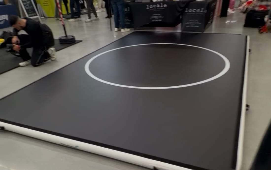 A 10 by 15 Pro FlowMat laid out on the floor of a busy expo hall, with vendor stands and a crowd behind it